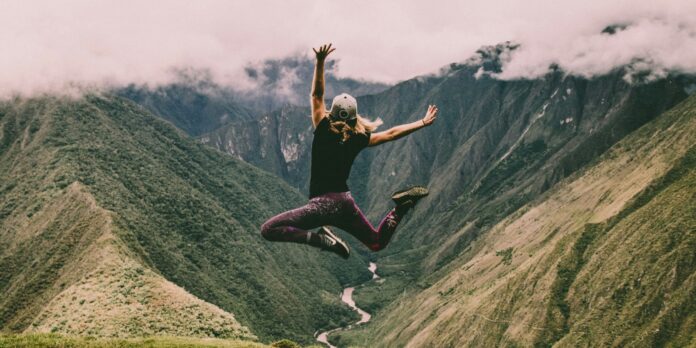 woman jumping on green mountains