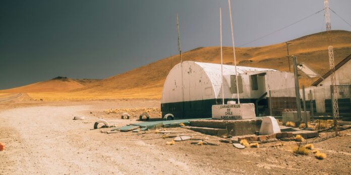 A dirt road next to a building and a red fire hydrant